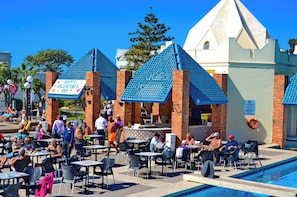 An outdoor pool area with tables and chairs, a sign reading 'Happy Valentine's Day,' and a building with a distinctive blue roof.