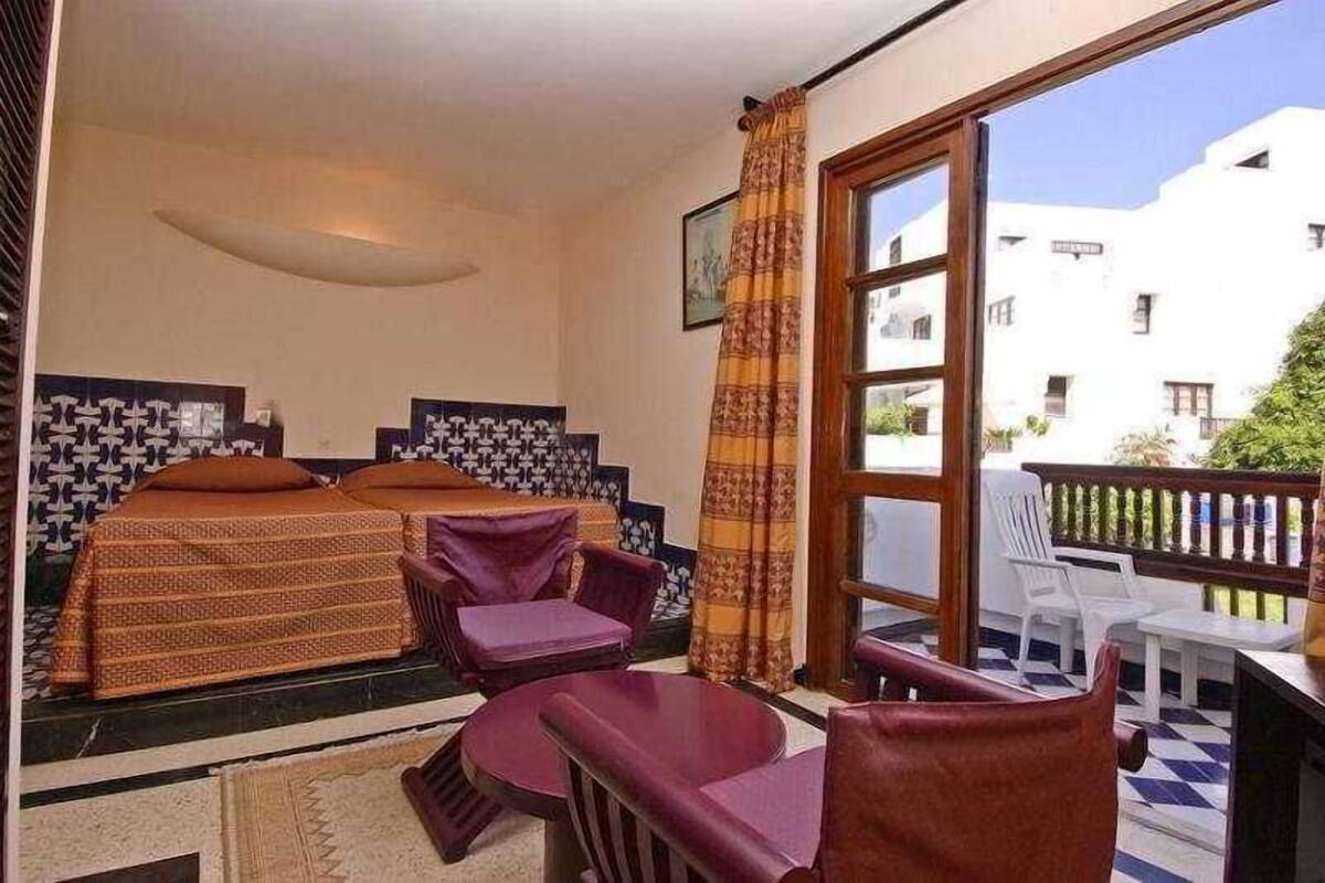 A hotel room with two beds, a balcony, and a view of buildings.