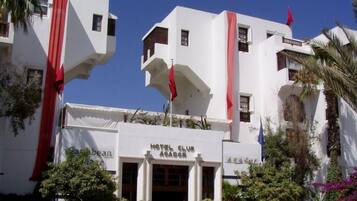 Un hotel con fachada blanca, detalles en rojo y un letrero que dice 'HOTEL CLUB AGADOR'.