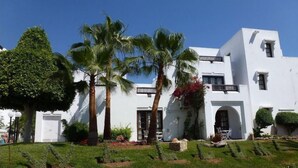 A white building with a balcony, palm trees, and a well-maintained garden. - Caribbean Village Agador (Agadir)