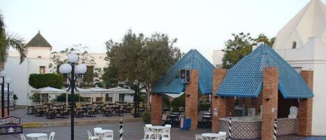 A courtyard with outdoor seating, a pool area, and a building with a distinctive blue roof.
