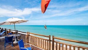 A beachside deck with a parasail, a table, chairs, and a view of the ocean. - Ocean Palace All Inclusive Premium (Natal)