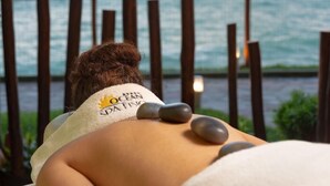 A person receiving a back massage with stones on their back, with a towel around their neck and a view of the ocean in the background. - Ocean Palace All Inclusive Premium (Natal)