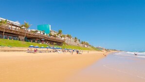 A beach with a hotel structure featuring a large blue building, palm trees, and beach umbrellas. - Ocean Palace All Inclusive Premium (Natal)