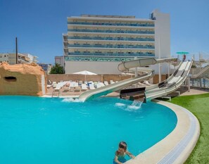 Una piscina con dos toboganes de agua, sillas de descanso y un edificio al fondo.