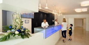 Un espace d’accueil doté d’un comptoir en verre, d’une réceptionniste et d’un espace d’attente agrémenté d’un grand arrangement floral.
