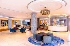 A spacious lobby with a central seating area, a reception desk, and a modern chandelier.