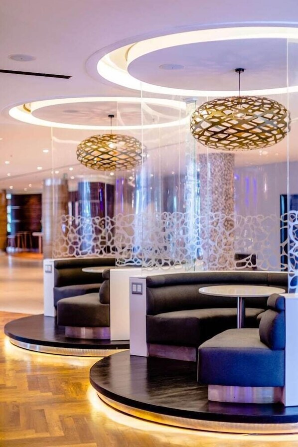 Un espacio de descanso moderno con plataformas circulares, una lámpara de techo con diseño y un muro decorativo.