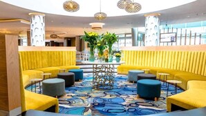 A modern lobby with yellow seating, a central table with plants, and unique hanging lamps. - Southern Sun Rosebank (Johannesburg)