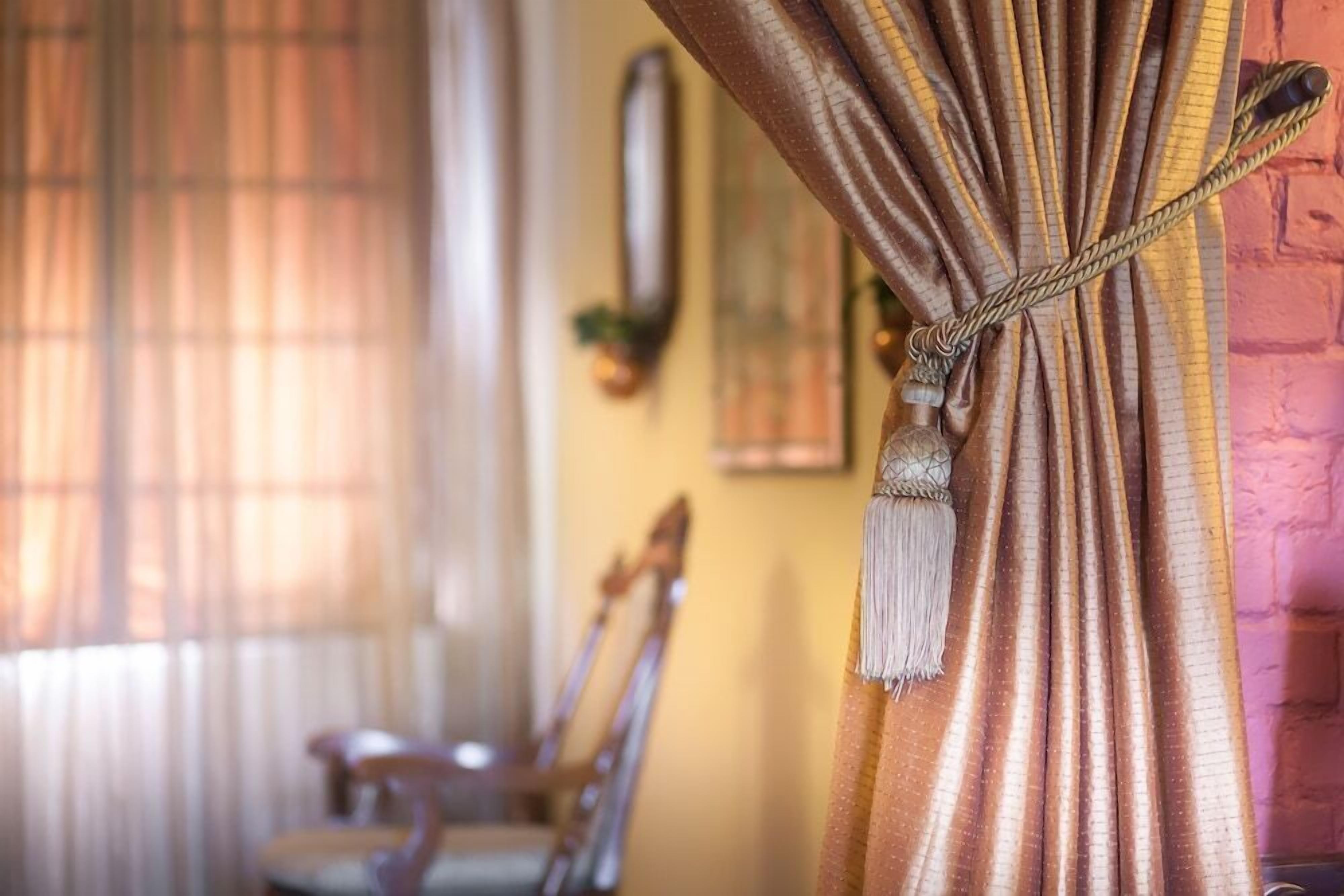 A room with a curtain tied with a tassel, a wooden chair, and a wall-mounted decoration.