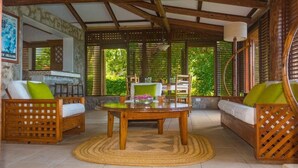 A cozy indoor space with a wooden table surrounded by wicker furniture, a woven rug, and a view of lush greenery outside. - Stonefield Estate Villa Resort (Soufrière)