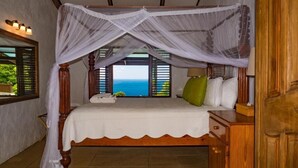 A four-poster bed with a canopy, a wooden nightstand, and a view of the ocean. - Stonefield Estate Villa Resort (Soufrière)