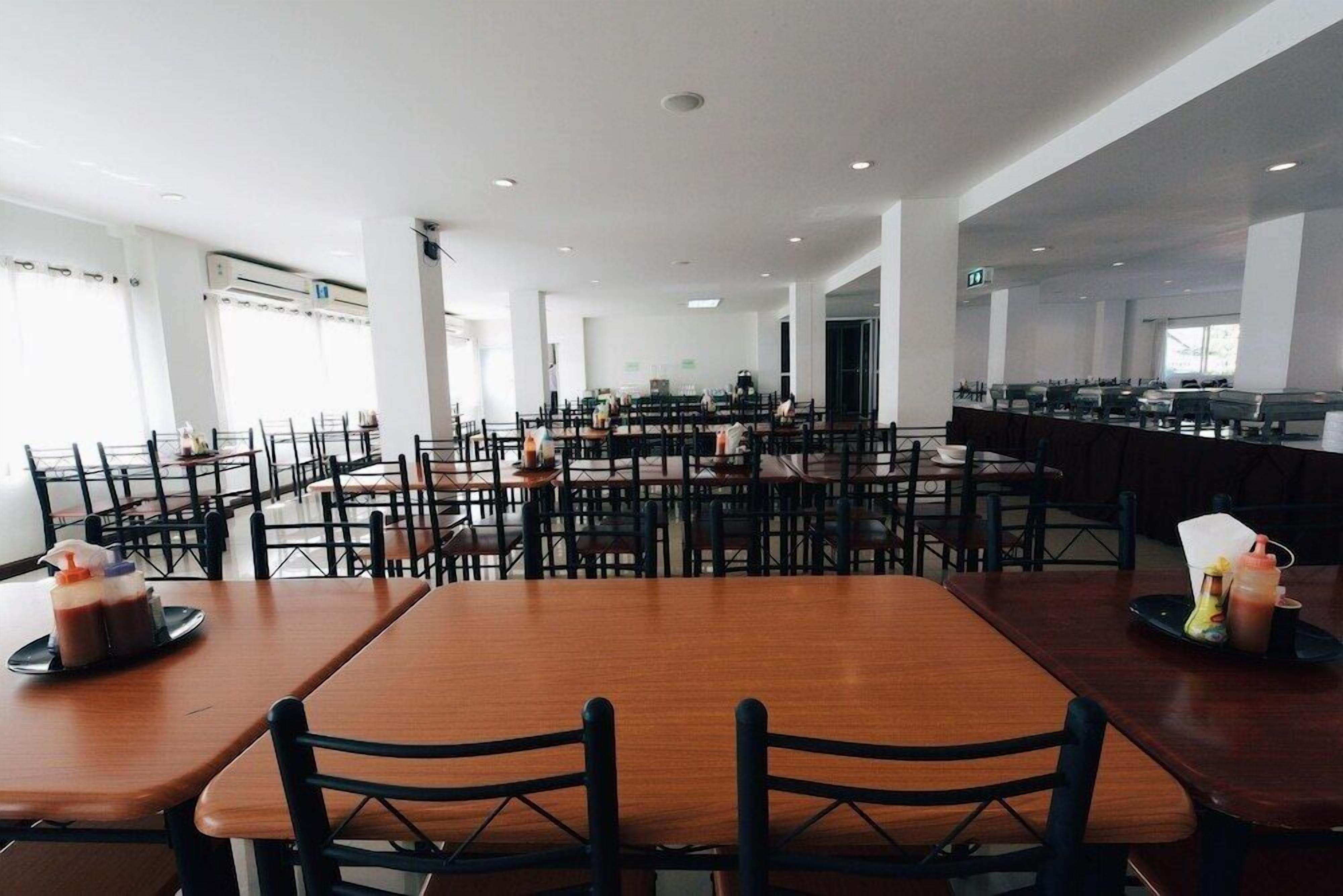 A spacious restaurant with multiple tables and chairs, a central bar area, and large windows allowing natural light.