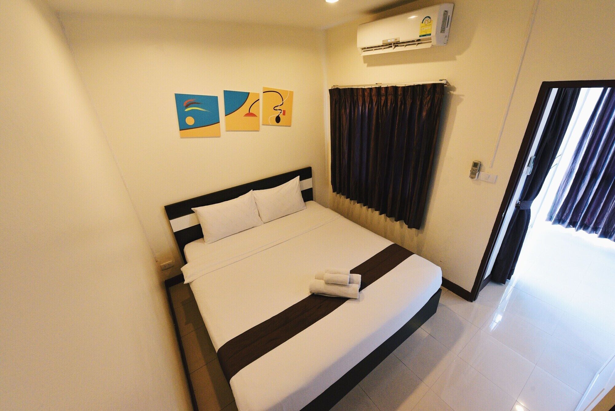 A hotel room with a bed, a wall-mounted air conditioner, and three artwork pieces.