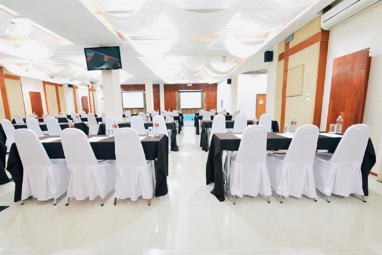 Un salón de conferencias con filas de mesas y sillas, una pantalla grande y un proyector.