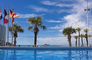 Una piscina con palmeras y banderas al fondo.