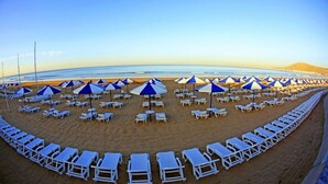 Una playa con hileras de sillas de descanso blancas y sombrillas azules, dispuestas en forma semicircular.