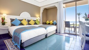 Habitación de hotel con dos camas, un balcón con vistas y zona de comedor.