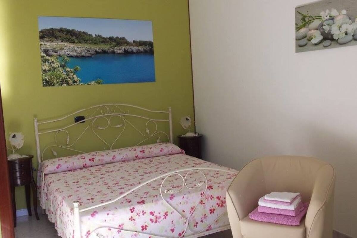 Une chambre à coucher comprenant un lit, une chaise, une table de chevet et un tableau accroché au mur.