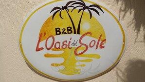Un senyal rodó amb un sol i palmeres, amb la inscripció 'B&B L'Oasi del Sole'.