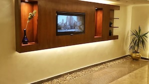 Una zona de recepción moderna con una televisión de pantalla plana montada en una pared de madera, rodeada de estanterías empotradas y una pequeña planta en maceta.