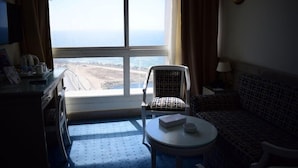 Una habitación de hotel con un ventanal grande, una silla, un sofá, una mesita y una lámpara.