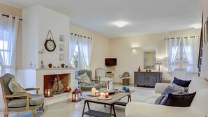 A living room with a fireplace, a television, and a dining table. - Villa Persephone (Kefalonia)