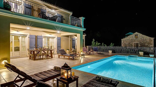 A swimming pool with lounge chairs and a dining area, surrounded by a stone building. - Villa Persephone (Kefalonia)
