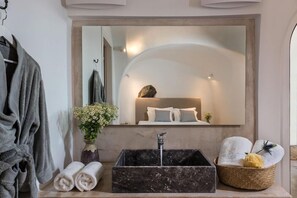 A bathroom with a large mirror, a marble sink, towels, and a decorative vase.