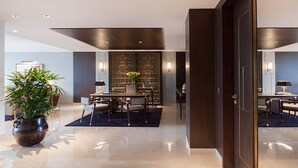 A modern hotel lobby with a dining area, a large potted plant, and a decorative wall.