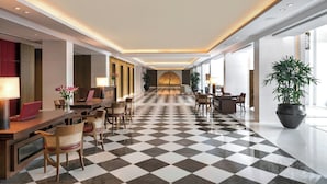 A hotel lobby with a checkered floor, wooden furniture, and a large potted plant.