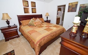 A bedroom with a wooden bed, two bedside tables, a nightstand, and a dresser. There are four framed pictures on the wall above the bed. - Vizcay Villa - Three Bedroom Home (Davenport)