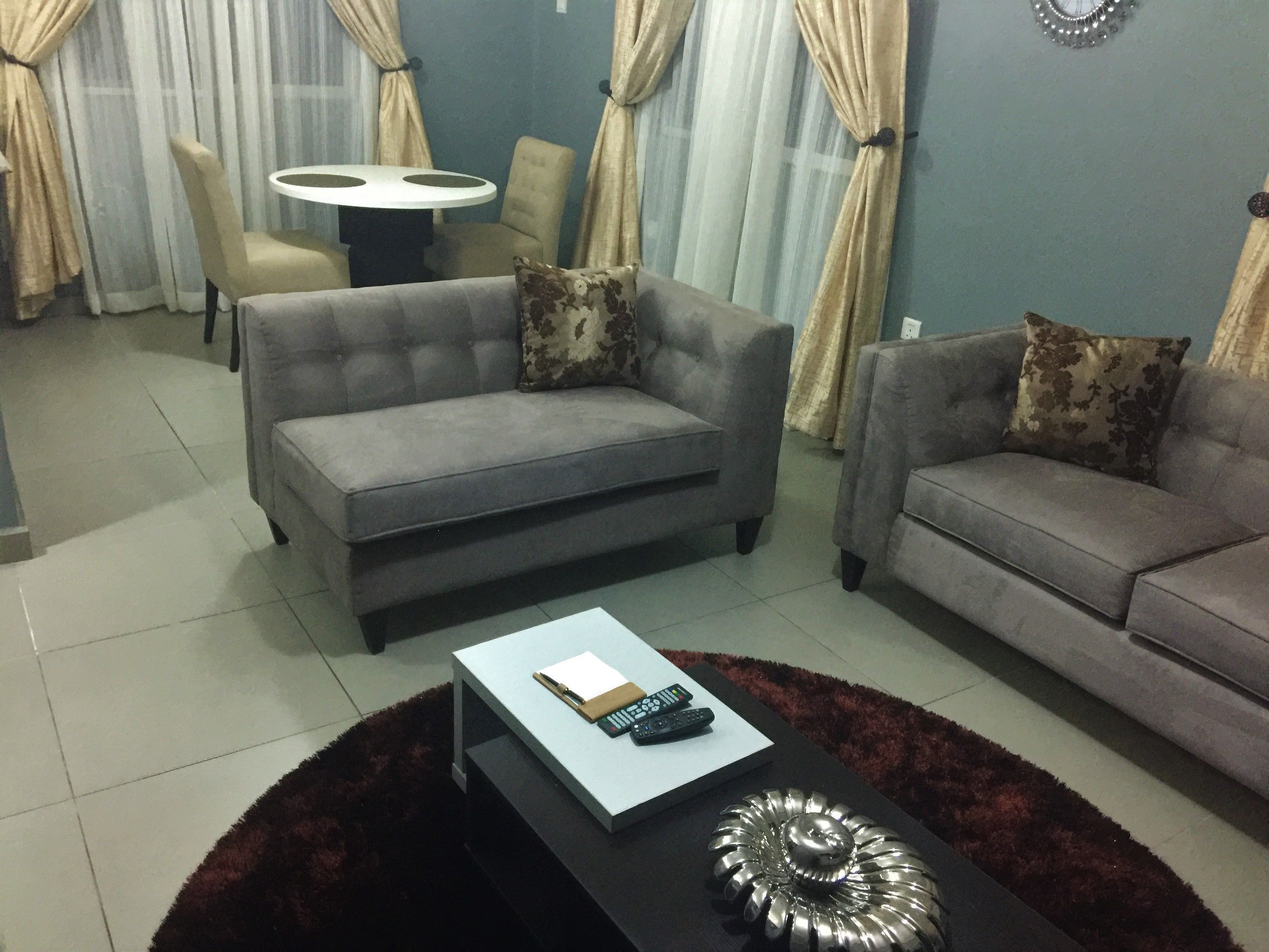 A living room with two grey sofas, a round coffee table with a decorative metal piece, and a small table with a book and remote controls.