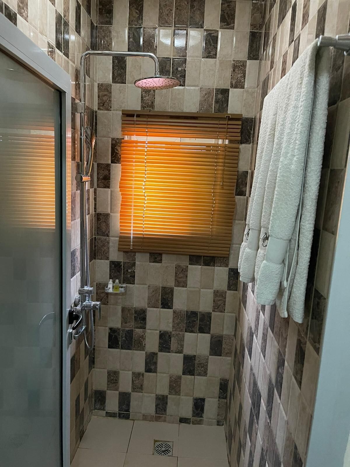 A bathroom with a shower, a window with blinds, and a towel rack.