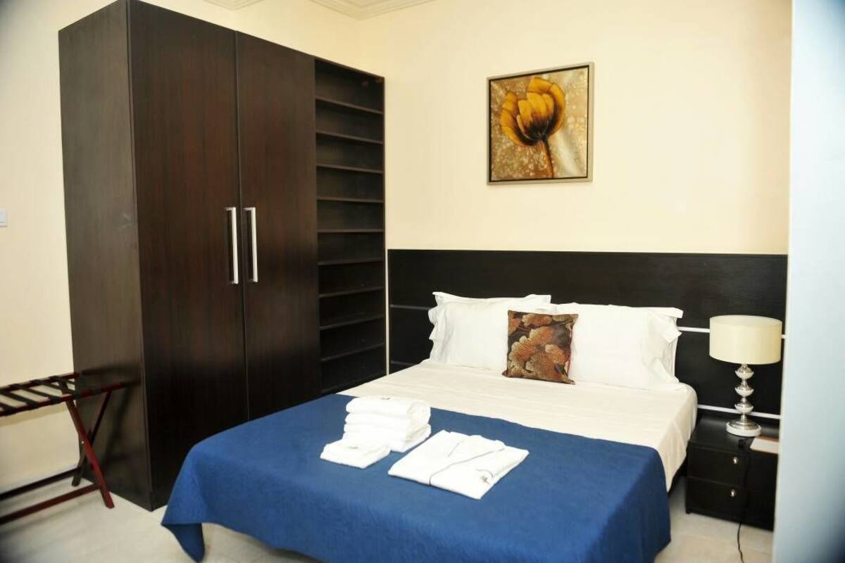 Una habitación de hotel con cama, armario, cuadro y mesita de noche.