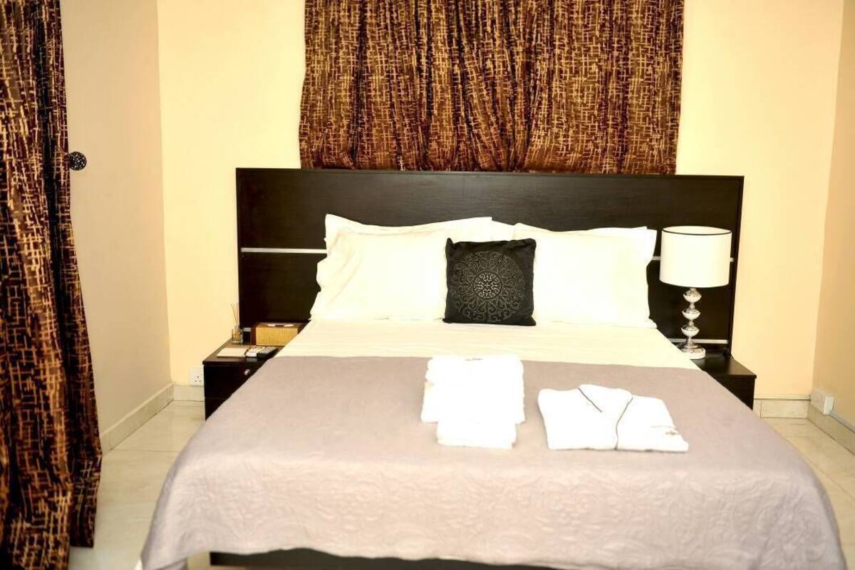 Una cama bien hecha con sábanas blancas, un cabecero negro y una lámpara de noche.