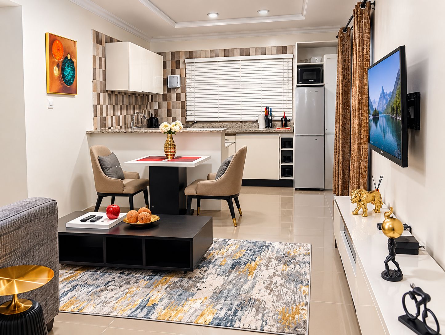 A modern kitchen with a dining area, a flat-screen TV mounted on the wall, and a decorative vase on the table.