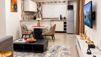 A modern kitchen with a dining area, a flat-screen TV mounted on the wall, and a decorative vase on the table.