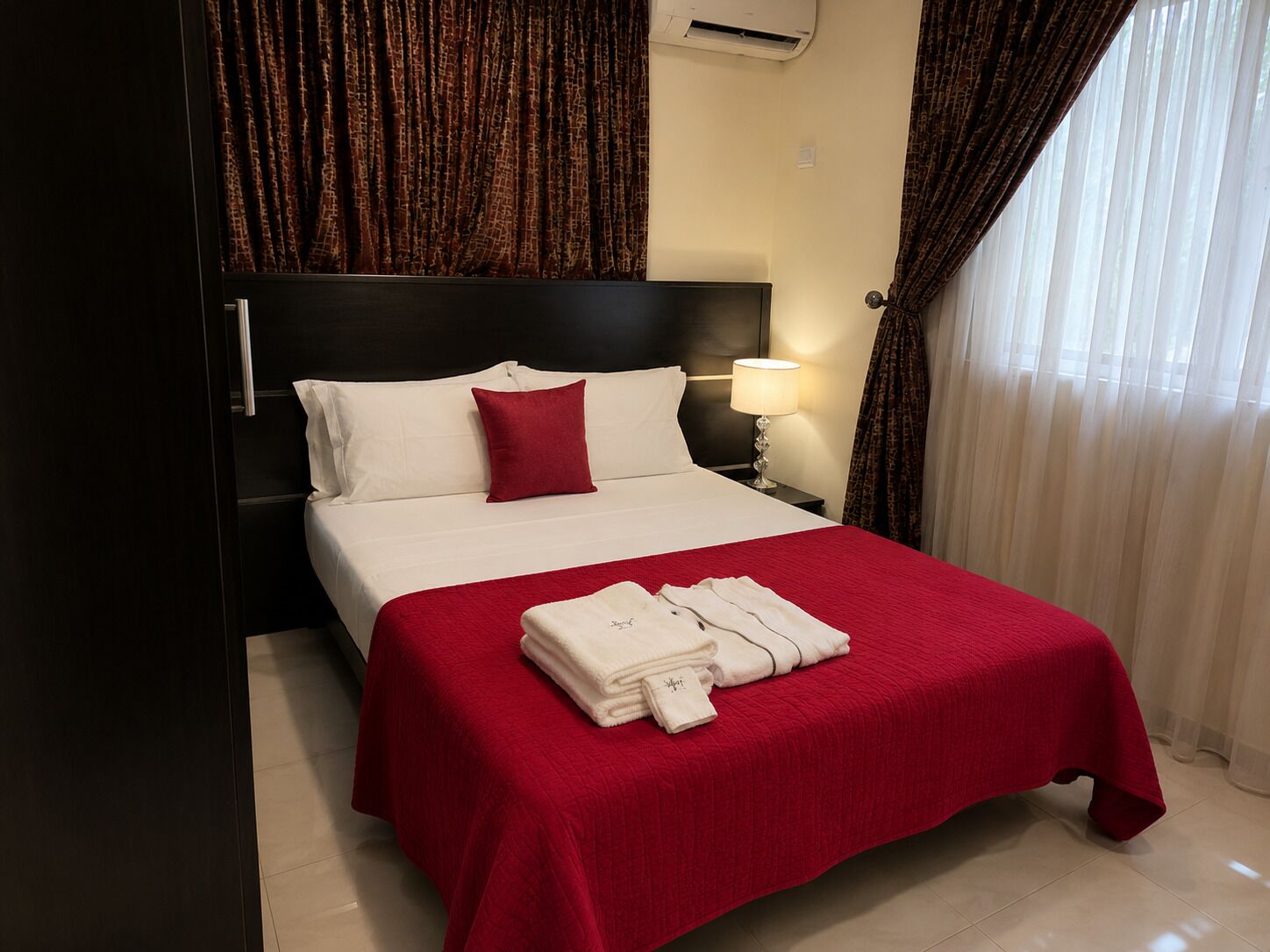 A hotel room with a bed, a nightstand, a lamp, and a window with curtains.