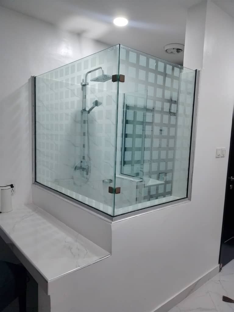 Een moderne badkamer met een douche met glazen wand, een wit marmeren aanrechtblad en een toilet.