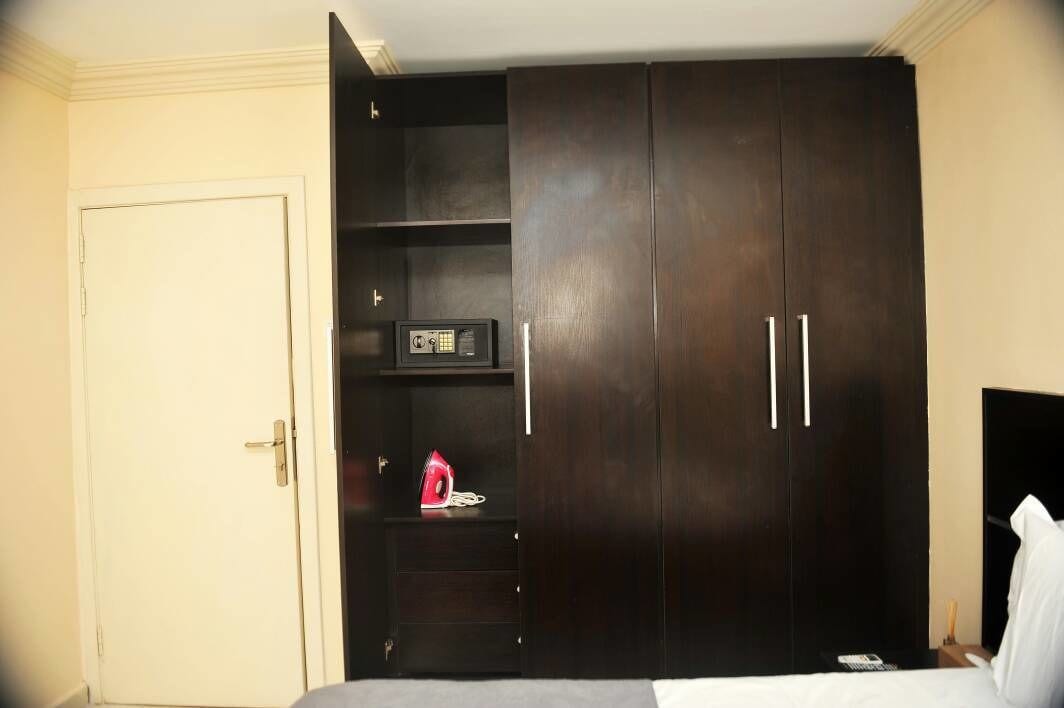 A bedroom with a dark wooden wardrobe, a bedside table with a lamp, and a bed.