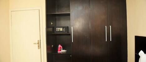 A bedroom with a dark wooden wardrobe, a bedside table with a lamp, and a bed.