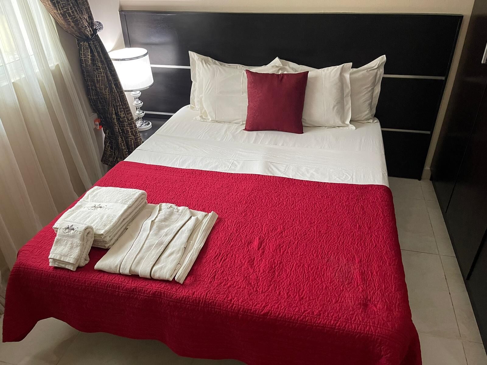 A hotel room with a bed, white bedding, a red blanket, and neatly folded white towels on the bed.