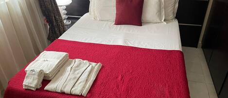 A hotel room with a bed, white bedding, a red blanket, and neatly folded white towels on the bed.