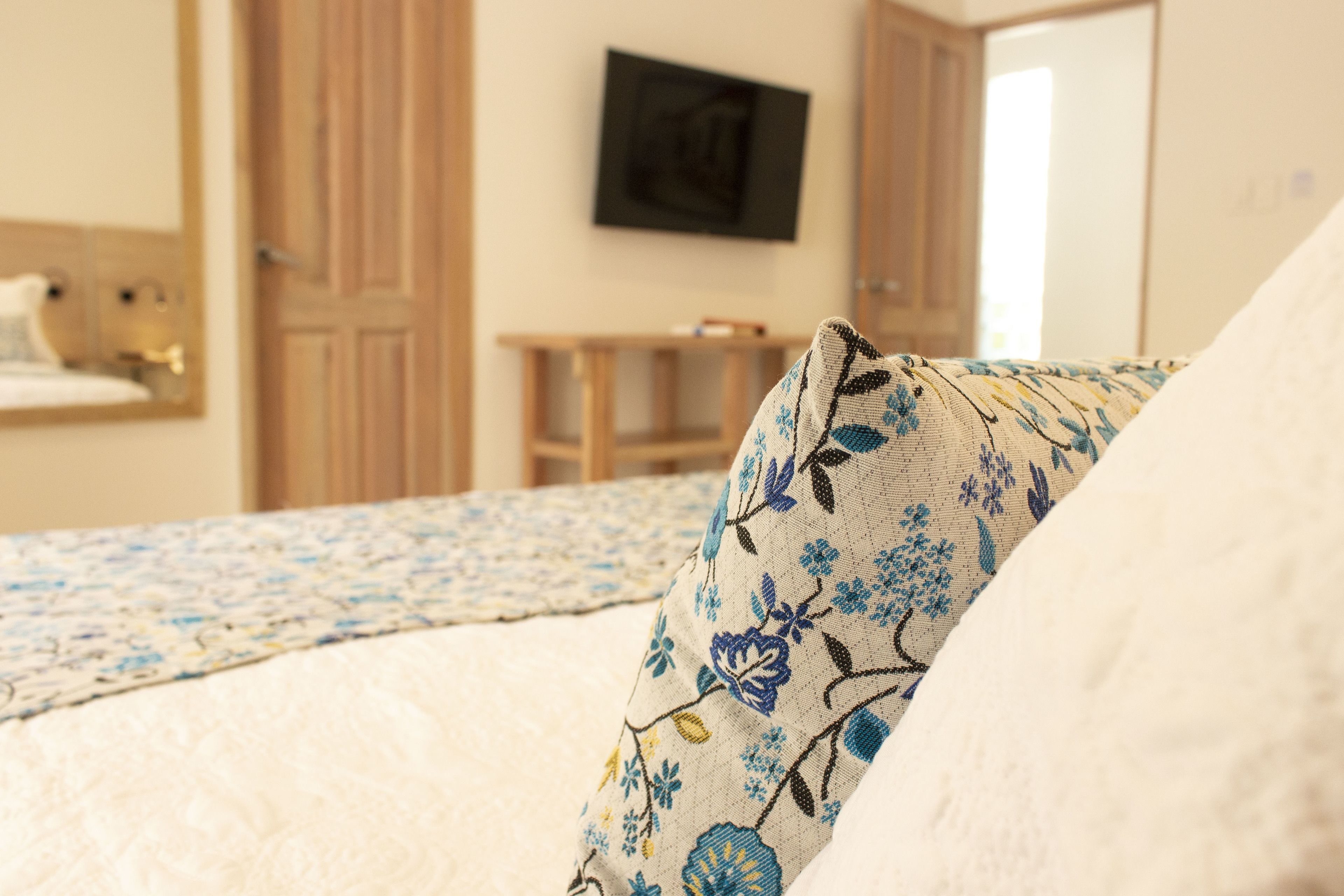 A bedroom with a bed, a wooden wardrobe, a television on the wall, and a small table.