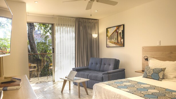 Une chambre d’hôtel avec un lit, un canapé, un bureau avec un ordinateur portable, un tableau au mur et une vue sur la verdure.