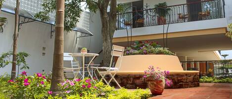 Un patio con zona de estar, una mesa y sillas, rodeado de exuberante follaje y plantas en flor.