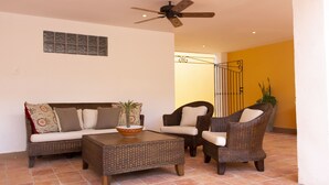 Un salon comprenant un canapé, deux fauteuils, une table basse, un ventilateur de plafond et un élément décoratif mural.