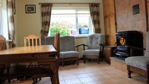 Un salon chaleureux avec une table en bois, deux fauteuils, une cheminée et une fenêtre avec des rideaux.