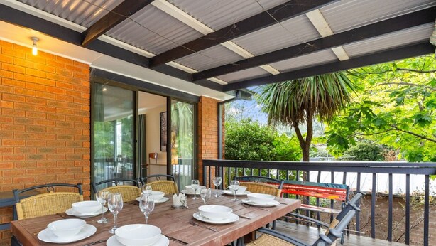 An outdoor dining area with a brick wall, glass doors, and a wooden table set for a meal.